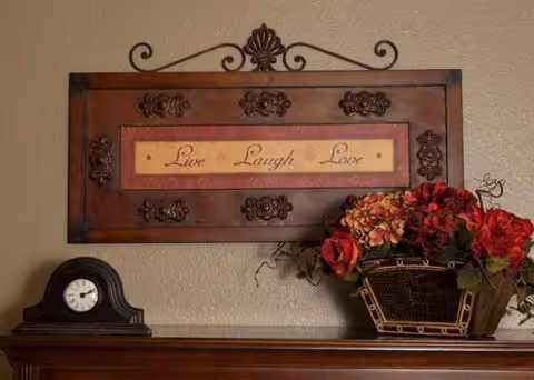 Decorative wall plaque reading Live Laugh Love above a mantel with a clock and flowers