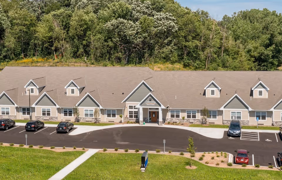 Single story senior living building with a curved driveway, parking lot, and landscaped front lawn.