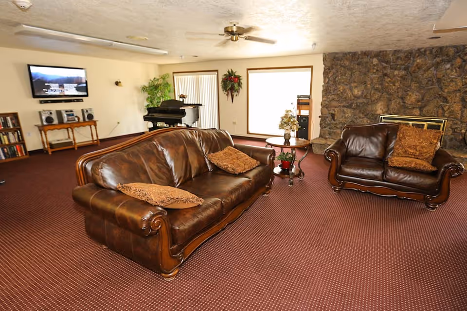 Spacious living room with brown leather sofas, a coffee table, TV, piano and a stone fireplace.