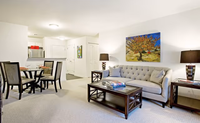 A furnished senior living room with sofa, coffee table, lamps, and a dining area.