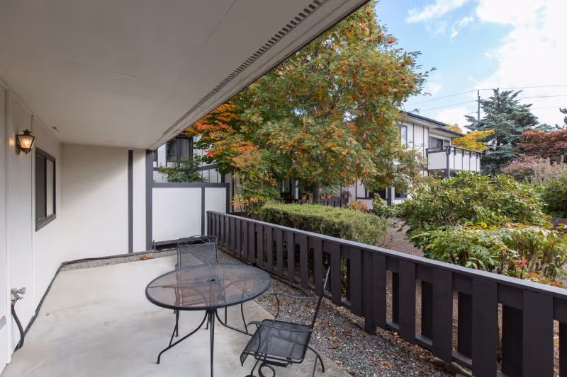 Covered ground-level patio with a metal table and chairs overlooking a landscaped courtyard and neighboring building.