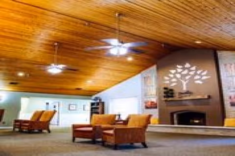 A spacious senior living lounge with wooden beamed ceiling, fans, and a fireplace.