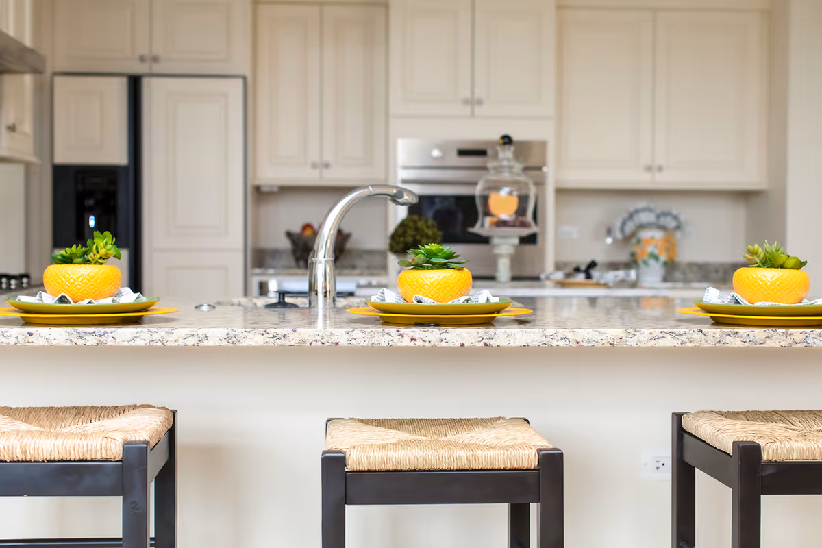 Modern kitchen island with three stools, a granite countertop and sink, and decorative yellow bowls with succulents.