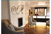 Modern reception area with a front desk, a staff member behind it, upholstered chairs, and decorative wall art.