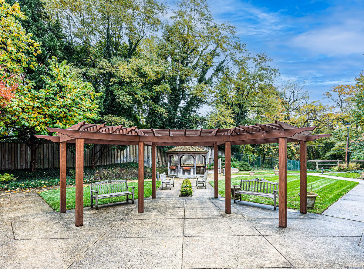 Wooden pergola with benches in a paved garden area.