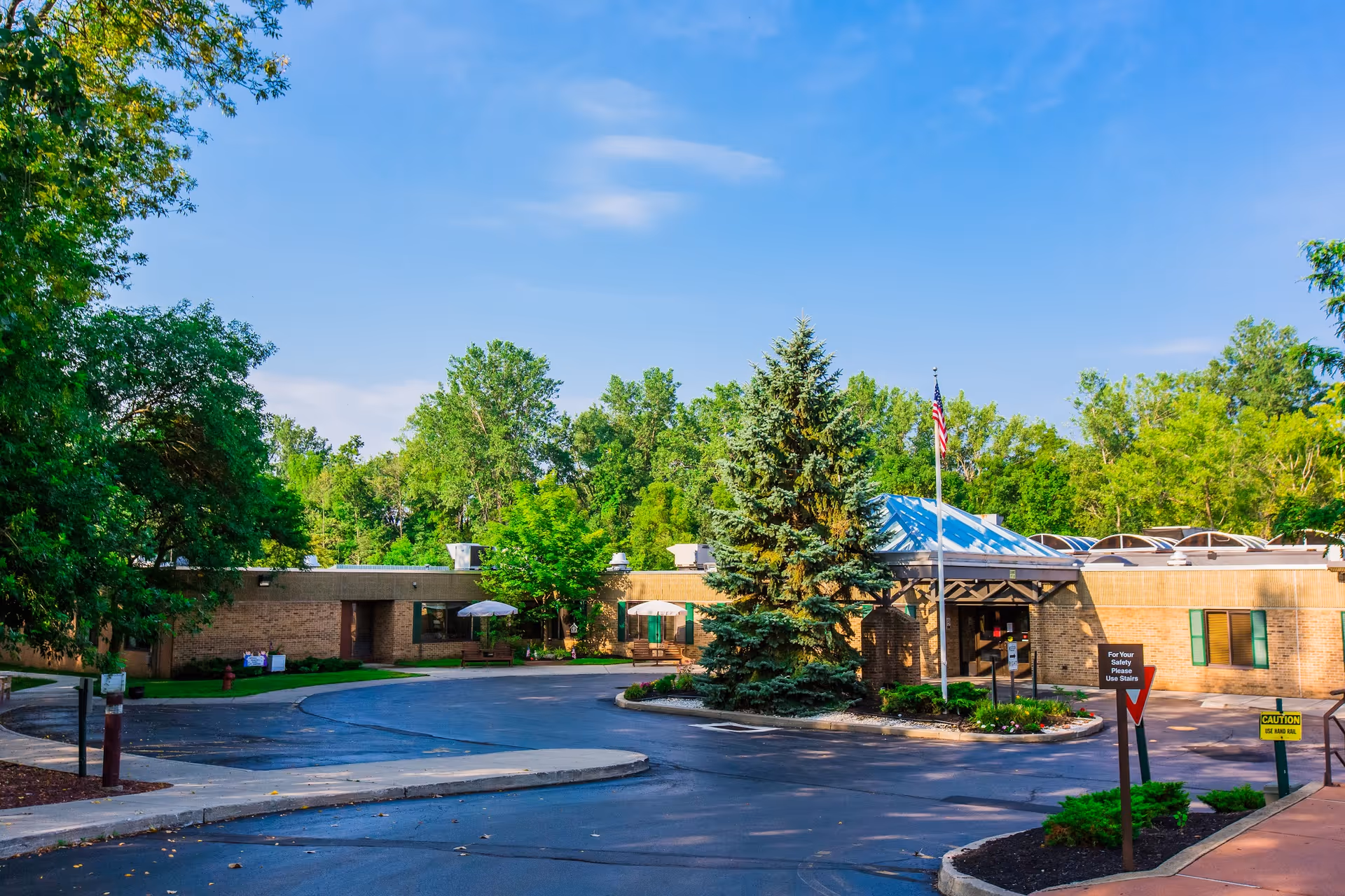 Exterior view of Seneca Health Care Center building surrounded by trees and greenery under a clear blue sky, with a paved driveway and an American flag near the entrance.