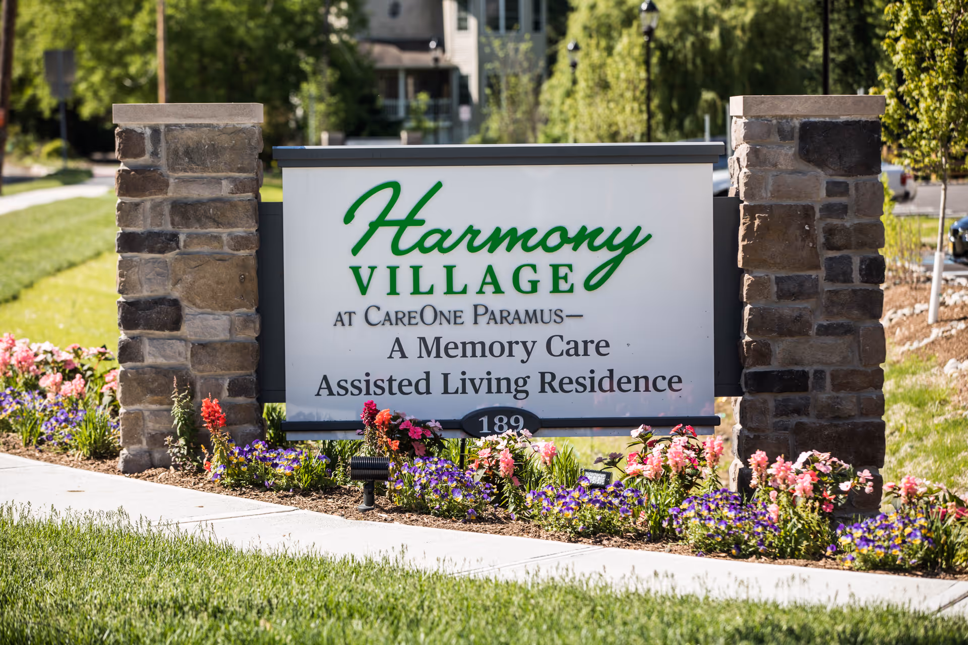 Entrance sign for Harmony Village at CareOne Paramus between stone pillars with flowers in front.