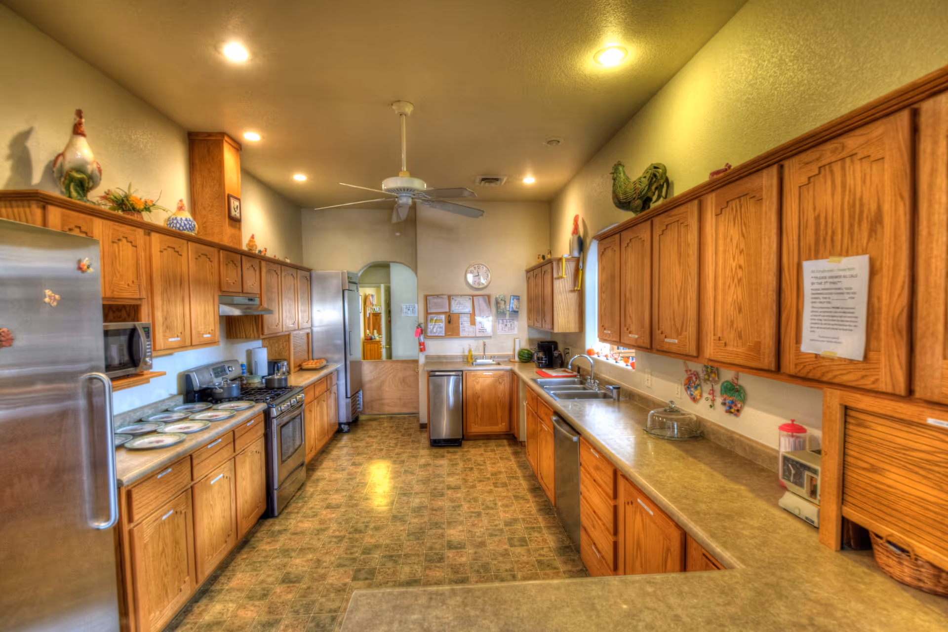 Spacious communal kitchen with wooden cabinets, stainless appliances, long countertops and a ceiling fan.