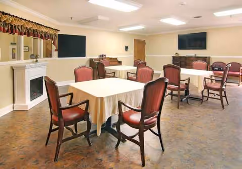 Senior living facility dining room with round tables, red chairs, and a fireplace.