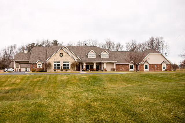 Front view of a single-story senior living building with a wide green lawn and leafless trees behind it.
