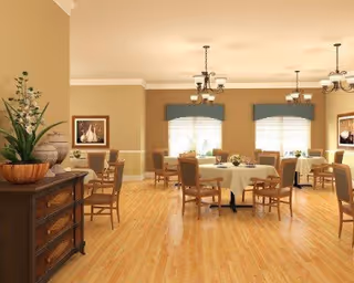 A spacious dining room with round tables covered with white tablecloths and surrounded by wooden chairs. The room has light wood flooring, beige walls, and three windows with blue valances letting in natural light. There are two chandeliers hanging from the ceiling and framed artwork on the walls. A wooden sideboard with decorative plants and bowls is visible on the left side.