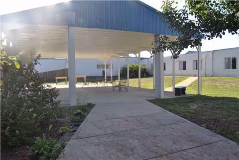 Outdoor covered seating area with tables and chairs beside a walkway at a senior facility