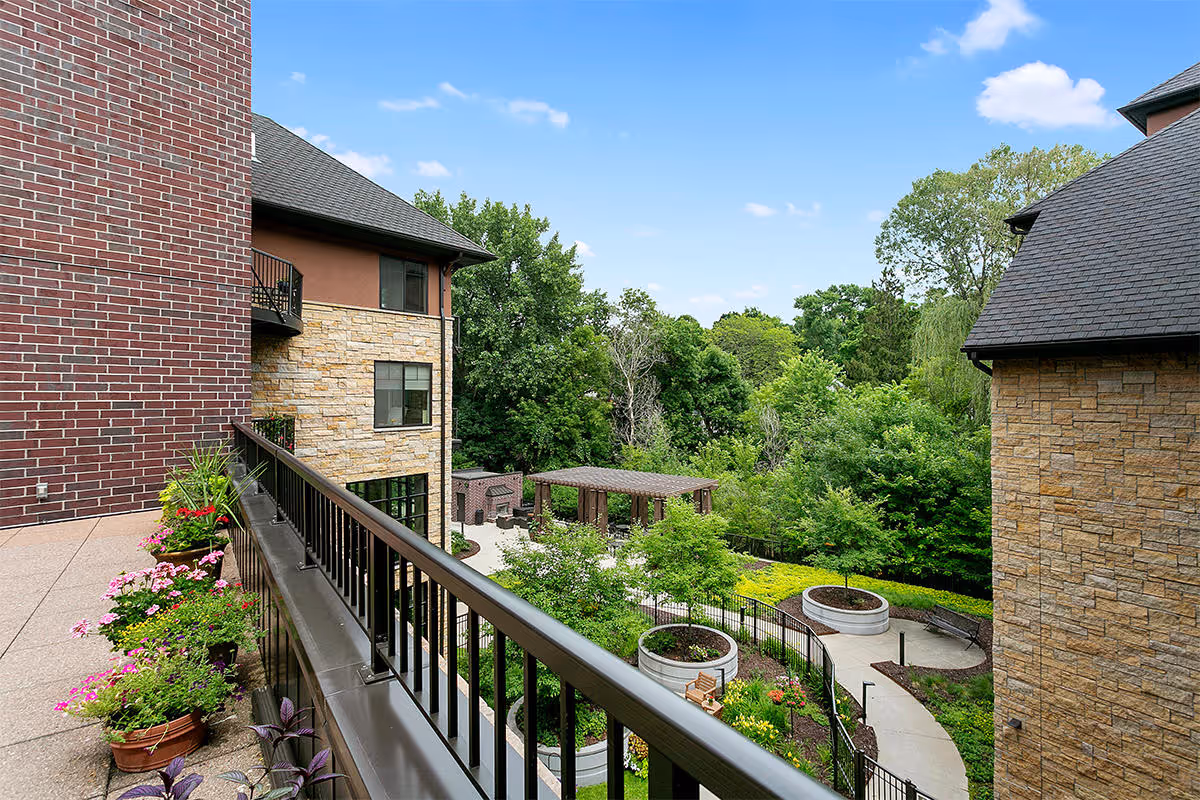 View from a balcony overlooking a landscaped courtyard with planters, winding paths, a pergola, and surrounding brick and stone buildings.