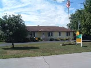Sunnyhills Residential Care Facility front with lawn, trees, and an American flag.