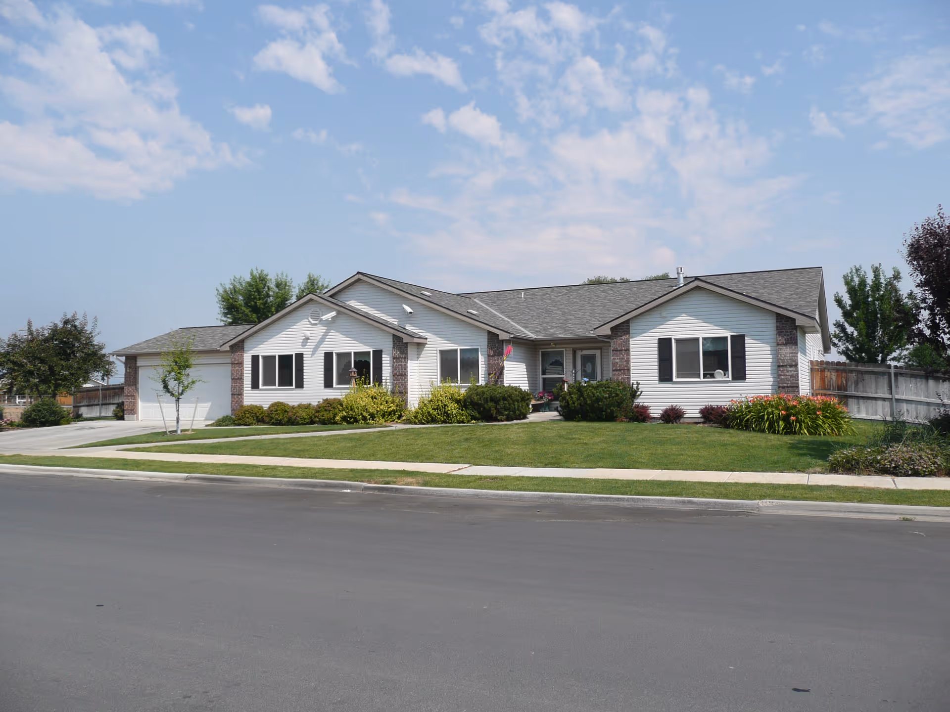 Single-story residential building with white siding and brick accents, surrounded by a well-maintained lawn and shrubs, under a partly cloudy blue sky.