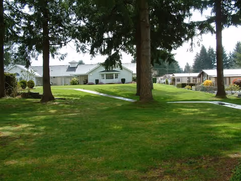 Grassy courtyard with tall trees and walkways leading to the front of low-rise retirement apartment buildings.