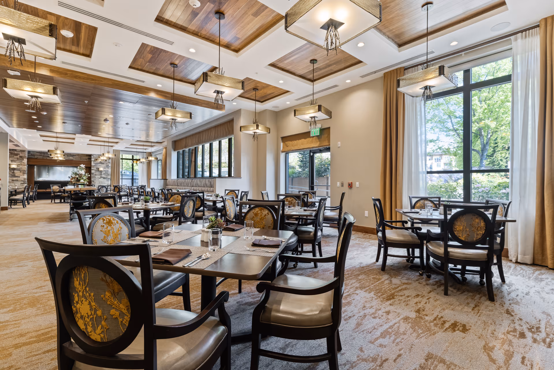 Bright, elegant dining room with multiple set tables, upholstered chairs, pendant lights, and large windows.