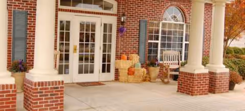 Brick front entrance with white double doors, columns, pumpkins, and hay bales on a welcoming porch.