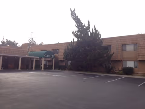 Exterior view of a single-story senior living facility with a large empty parking lot.