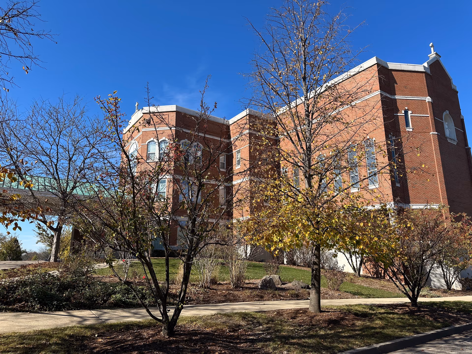 Exterior view of a large brick building with multiple windows and decorative architectural elements, surrounded by trees with autumn foliage and a clear blue sky.