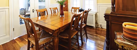 Wooden dining table with six chairs in a bright dining room with hardwood floors and a sideboard.
