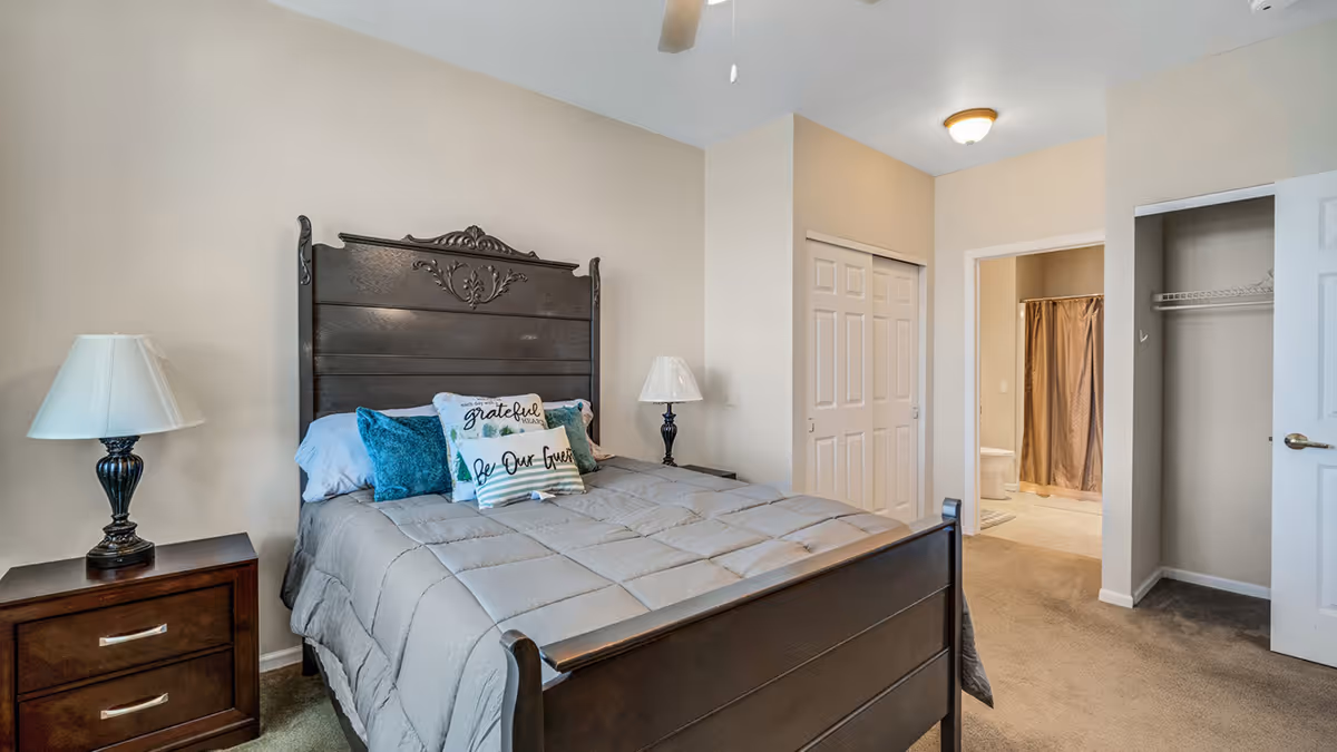 Neatly furnished bedroom with a dark wooden bed, nightstands with lamps, a closet, and a view into an en-suite bathroom.