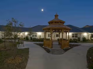 Front view of Aberdeen Memory Care of Tulsa with a wooden gazebo and lit building facade.