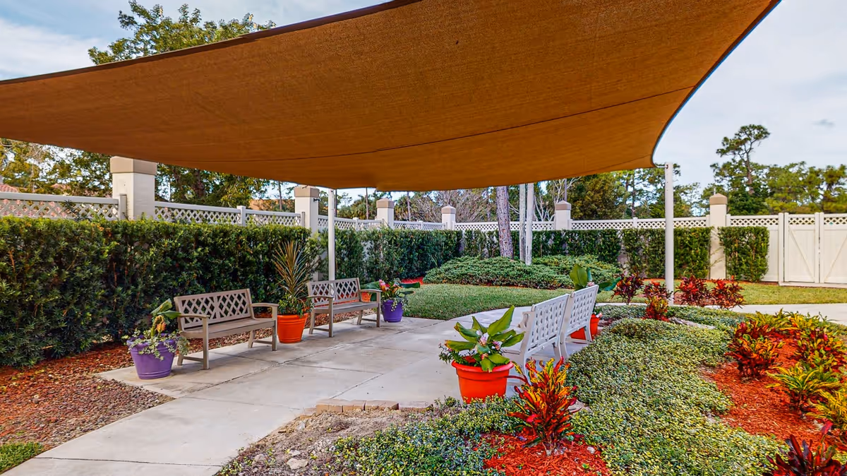Shaded outdoor courtyard with benches and colorful potted plants beneath a large canopy.