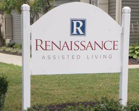 A white sign with Renaissance Assisted Living logo stands in front of a green lawn.