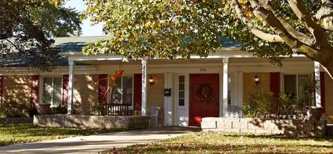 Front exterior of a senior living facility with red doors and potted greenery.
