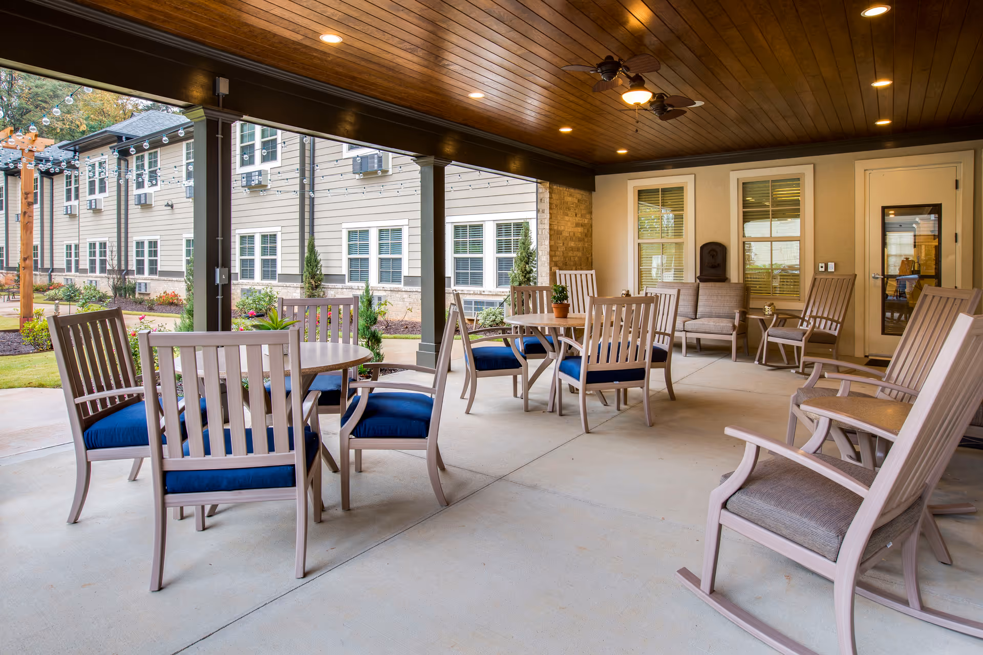 Covered outdoor patio area with tables, chairs, and ceiling fans overlooking landscaped grounds.