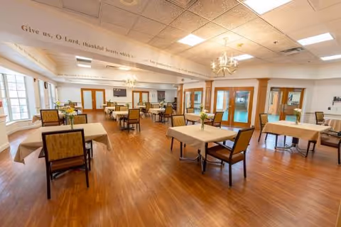 Spacious dining room with multiple tables and chairs, chandeliers, wood floors, and large windows.