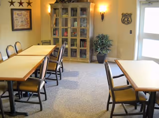 Small dining area with tables and chairs, a glass-front cabinet, wall decorations and a potted plant near a door.