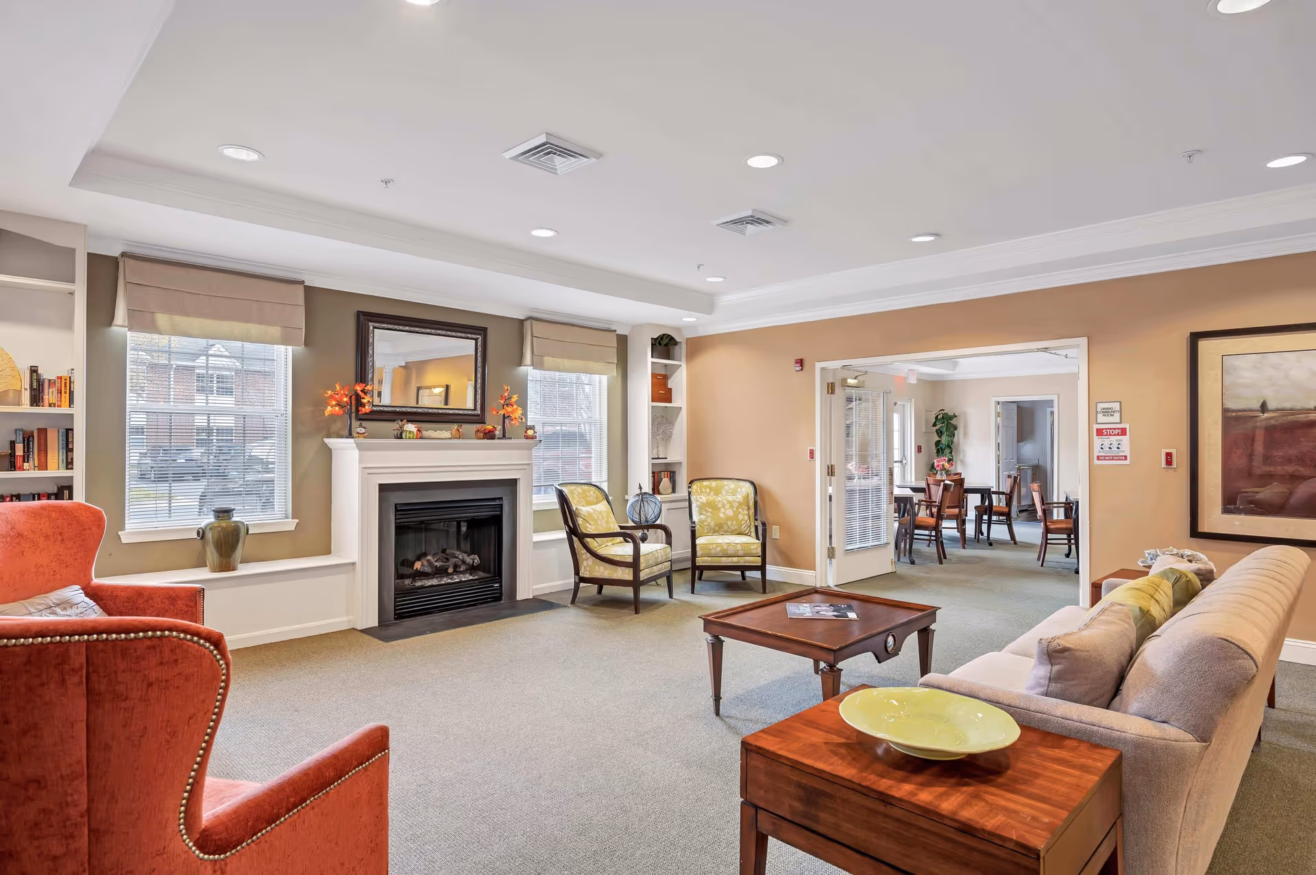 Communal living room with a fireplace, couches and chairs arranged around a coffee table and a view into an adjacent dining area.