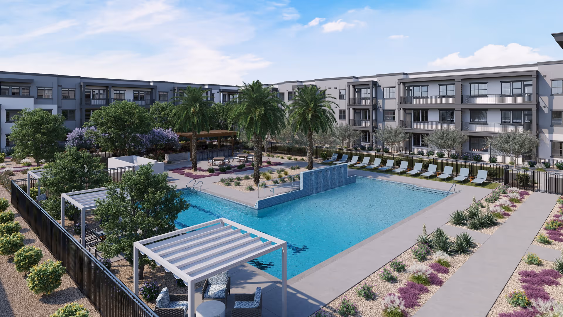 Outdoor view of a senior living facility featuring a large swimming pool with a waterfall wall, surrounded by lounge chairs and palm trees. There are pergolas with seating areas and landscaped gardens with various plants and shrubs. The multi-story residential building is visible in the background under a partly cloudy sky.