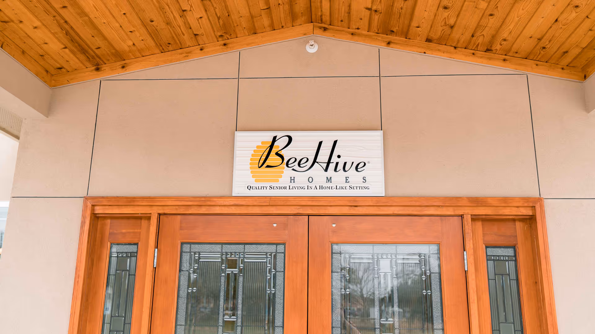 Front entrance with wooden double doors and a BeeHive Homes sign mounted above under a wood-paneled overhang.