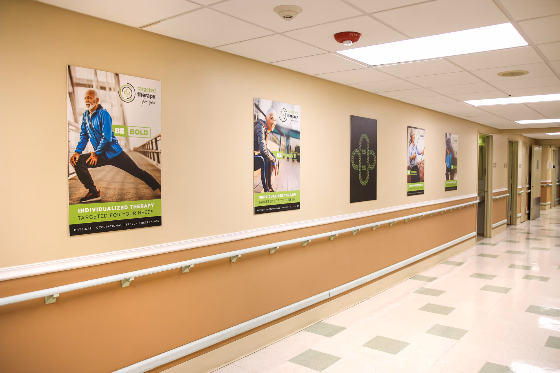 A long, well-lit hallway in a care facility with handrails on both sides and motivational posters on the walls promoting individualized therapy. The floor has a tiled pattern and several doors line the hallway.