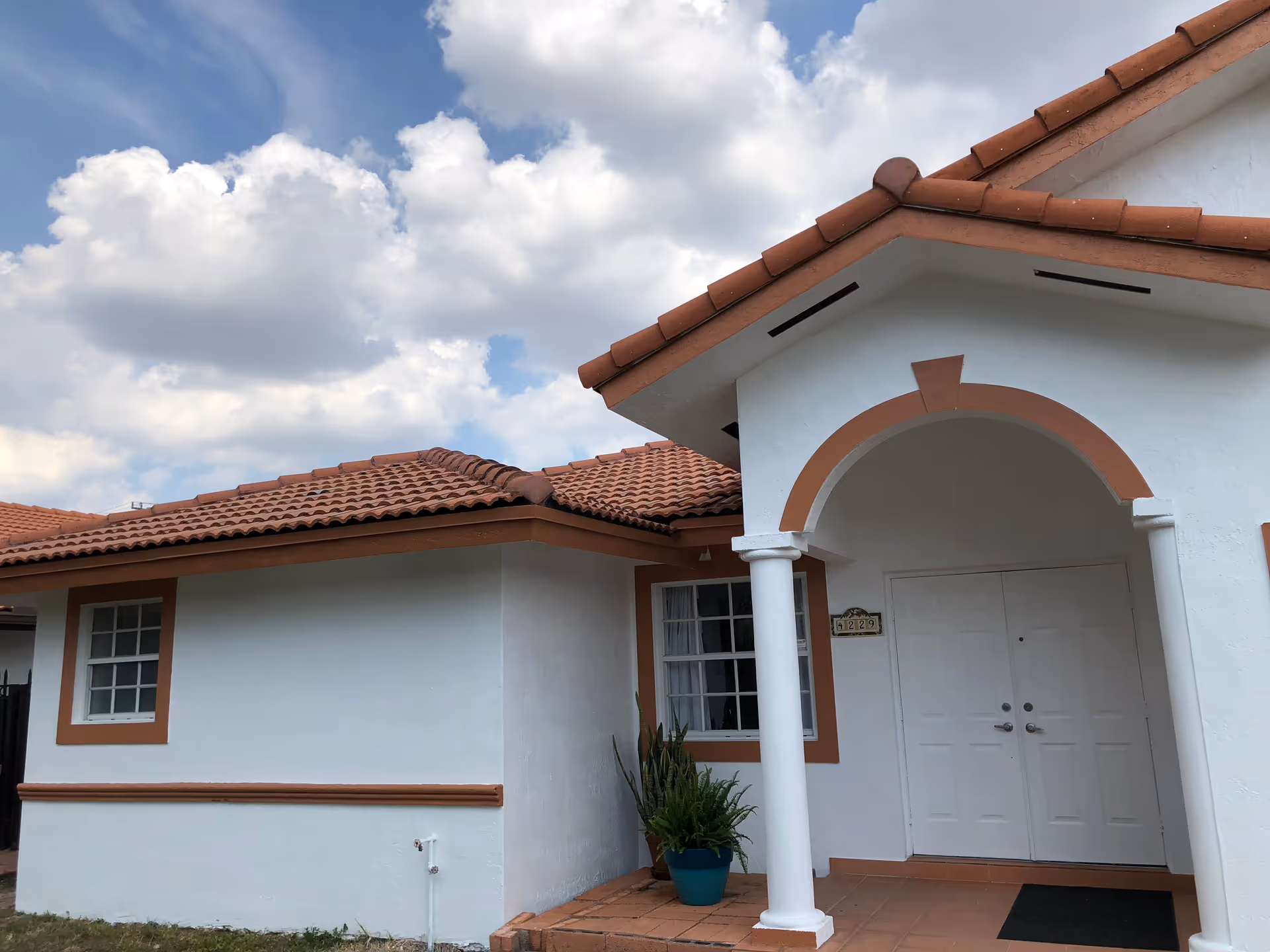 White building with red-tiled roof, arched entrance, and columns.