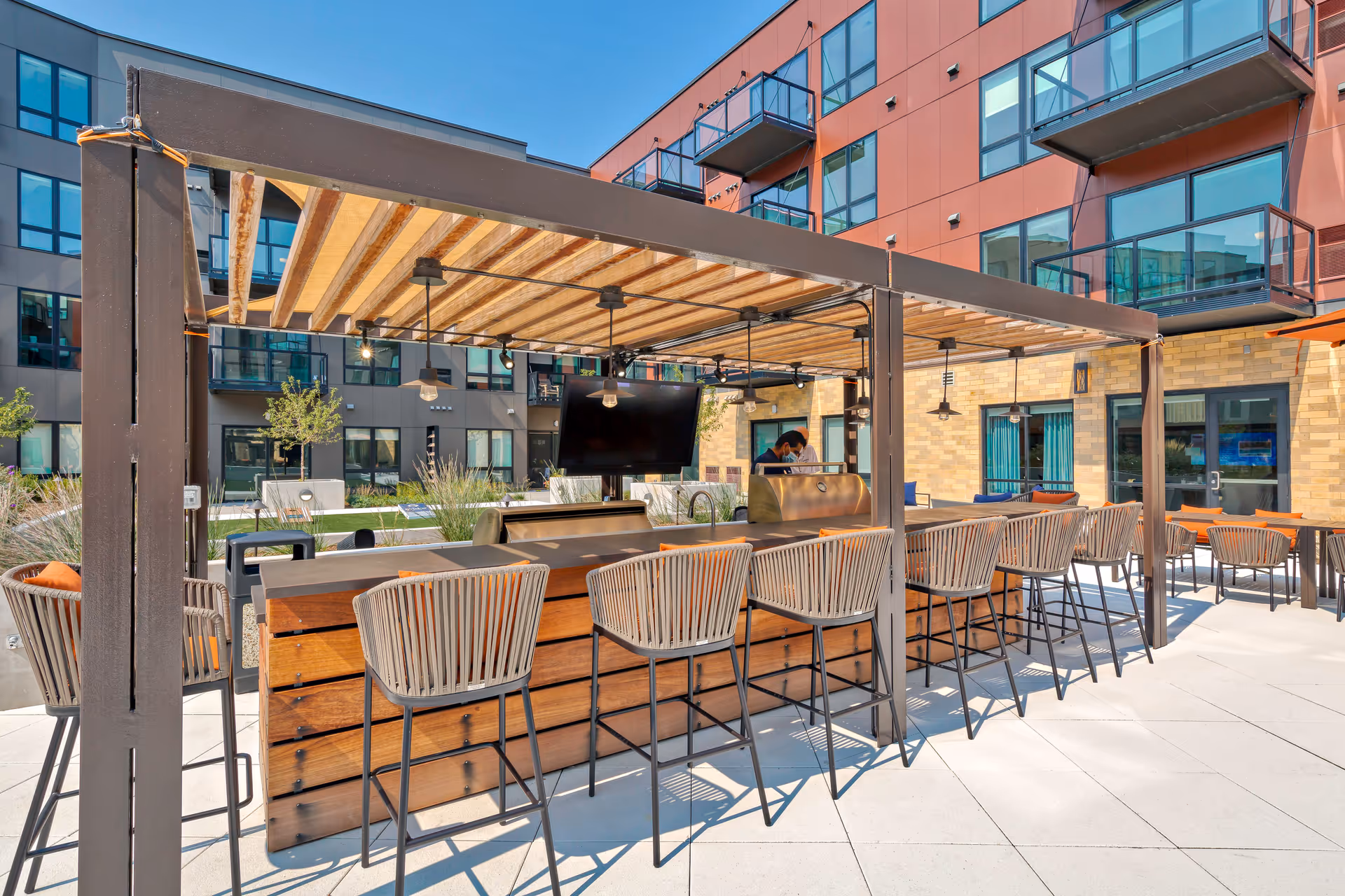 Outdoor communal bar with high stools under a pergola in the courtyard of a modern apartment building.