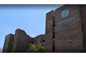 Brick multi-story nursing and rehabilitation facility exterior showing a green circular logo and 'PENINSULA' signage against a clear blue sky.