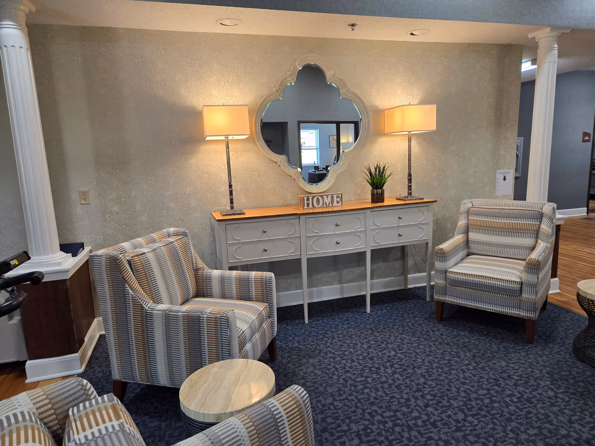 Cozy lounge area with striped armchairs, a console table topped with lamps, mirror and a "HOME" sign.