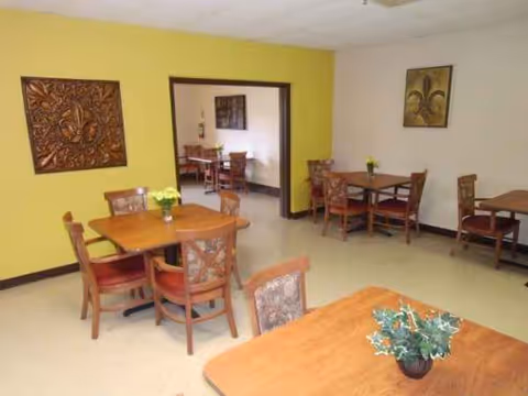 Yellow-walled dining area with several wooden tables and chairs, decorative artwork on walls.