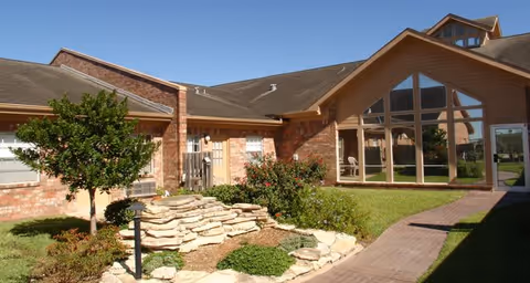 Exterior view of a single-story brick building with large triangular windows, a small landscaped garden with rocks and plants, and a paved walkway under a clear blue sky.