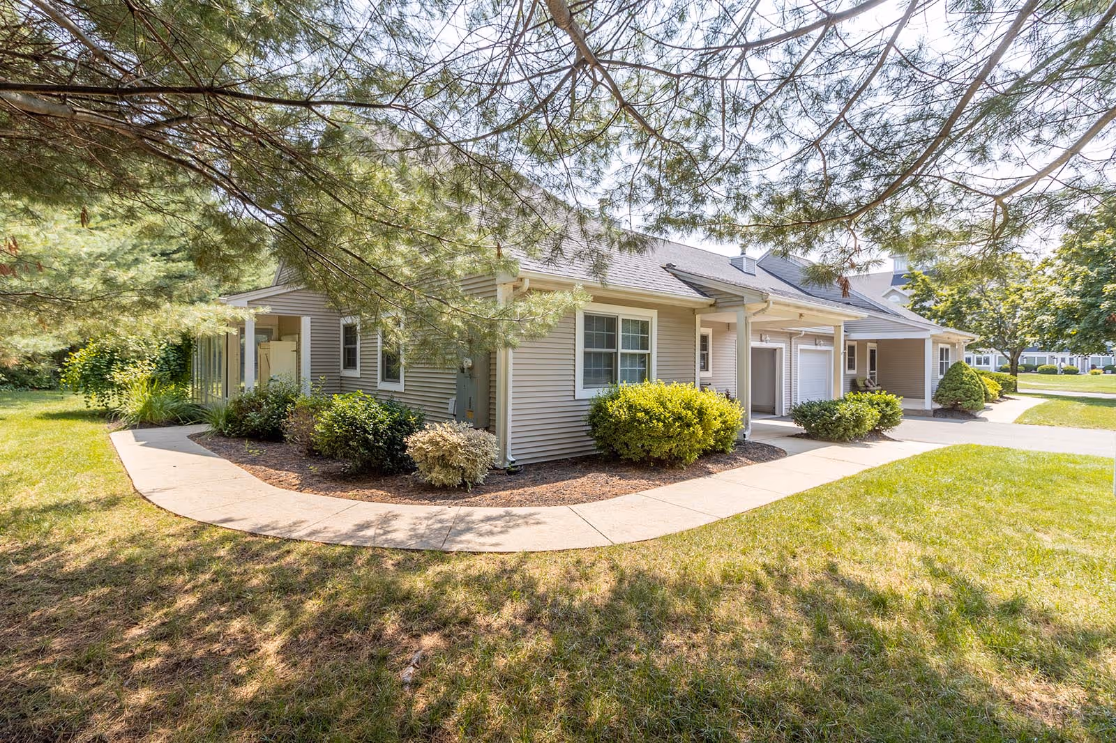 Low single-story residential building with covered entrances, garages and a curved walkway amid landscaped lawns and trees.