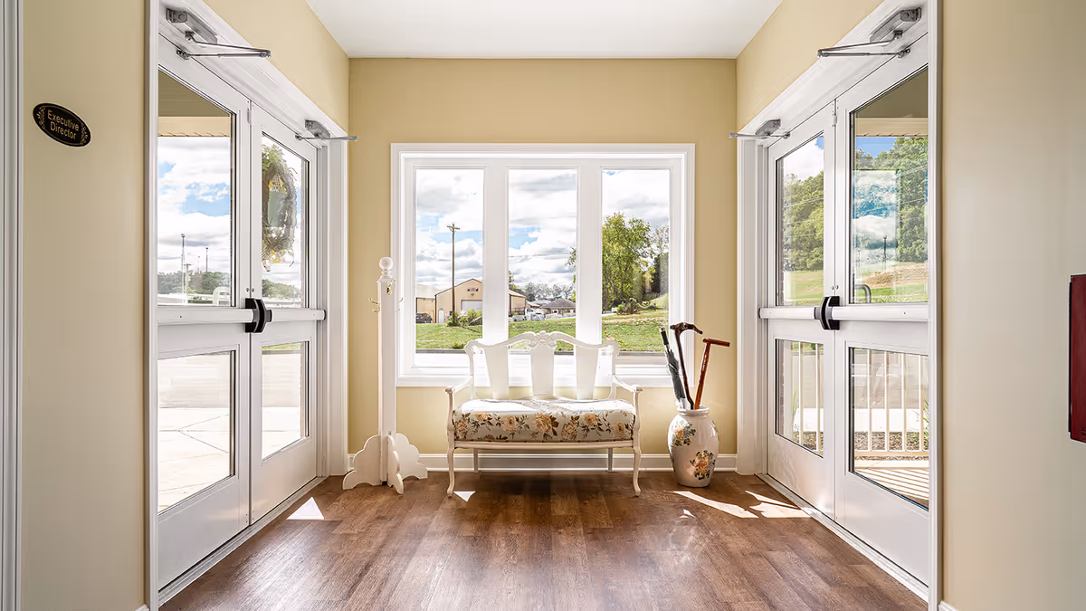 Bright entryway with a floral bench centered beneath a large window, flanked by glass double doors and an umbrella/cane stand.