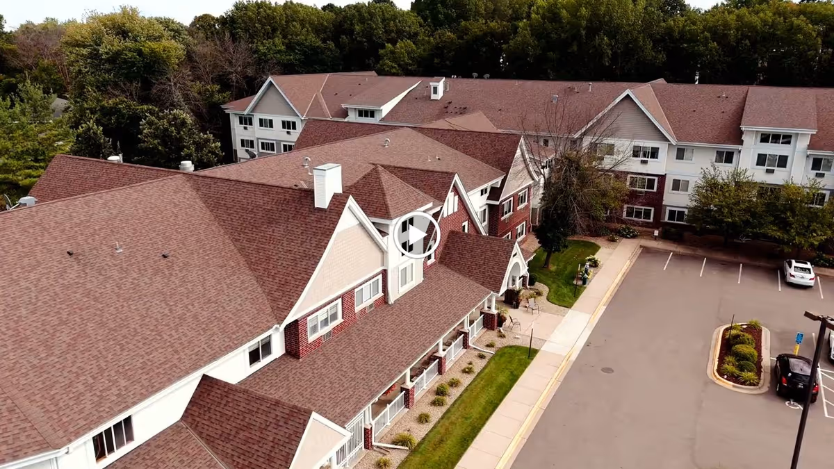 Aerial view of New Perspective Senior Living | Prior Lake building with multiple connected sections, red roofs, white and brick exterior walls, surrounded by trees and a parking lot with a few cars.