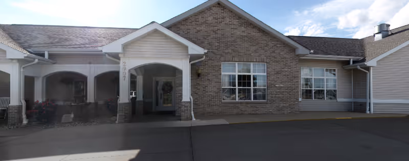 Front entrance of a senior living building with a covered portico, brick facade, and large windows.