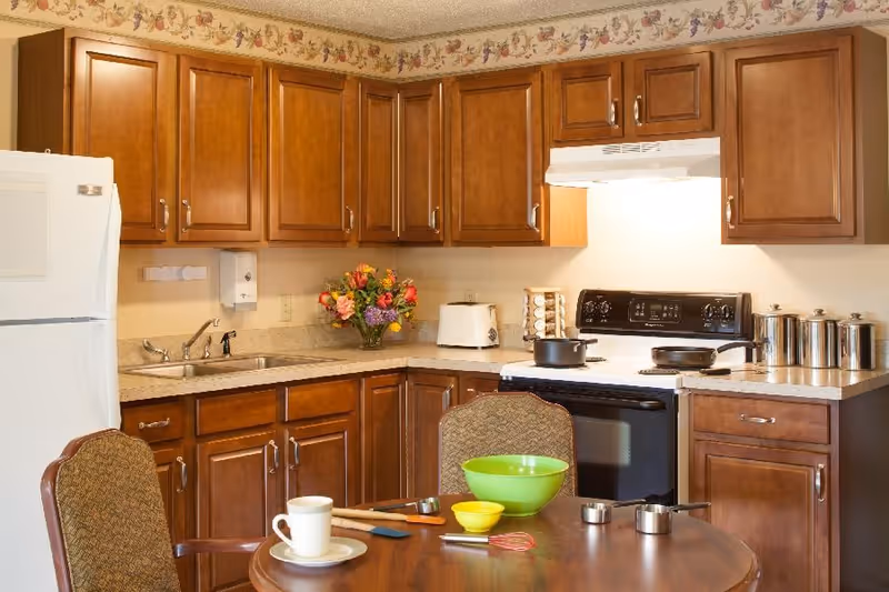 Cozy kitchen with wooden cabinets, white refrigerator and stove, and a round table set with bowls and a mug.