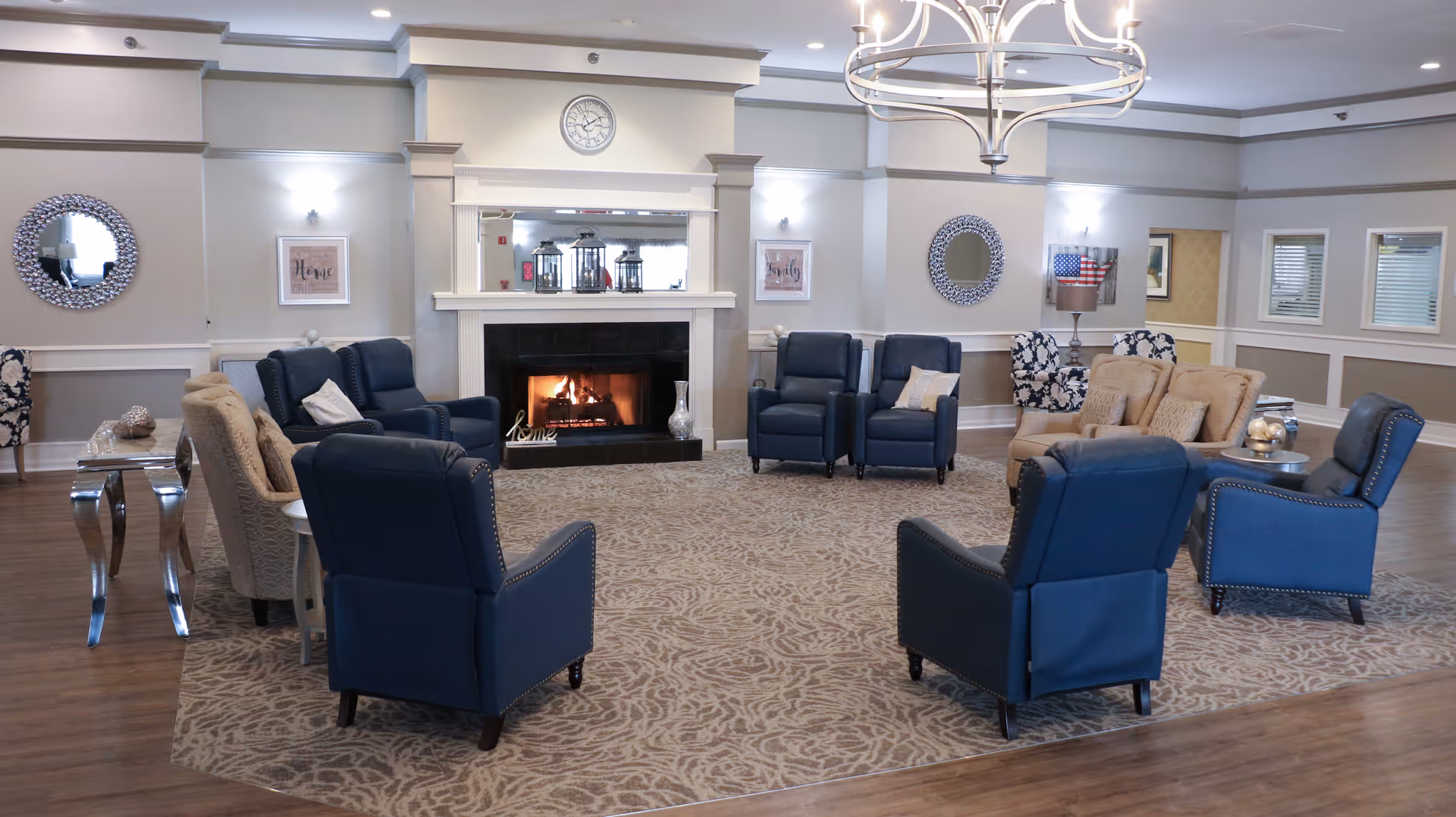 Spacious communal lounge with a central fireplace, multiple upholstered armchairs, and a chandelier.