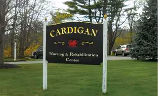A black Cardigan Nursing and Rehabilitation Center sign on white posts on a grassy front lawn.